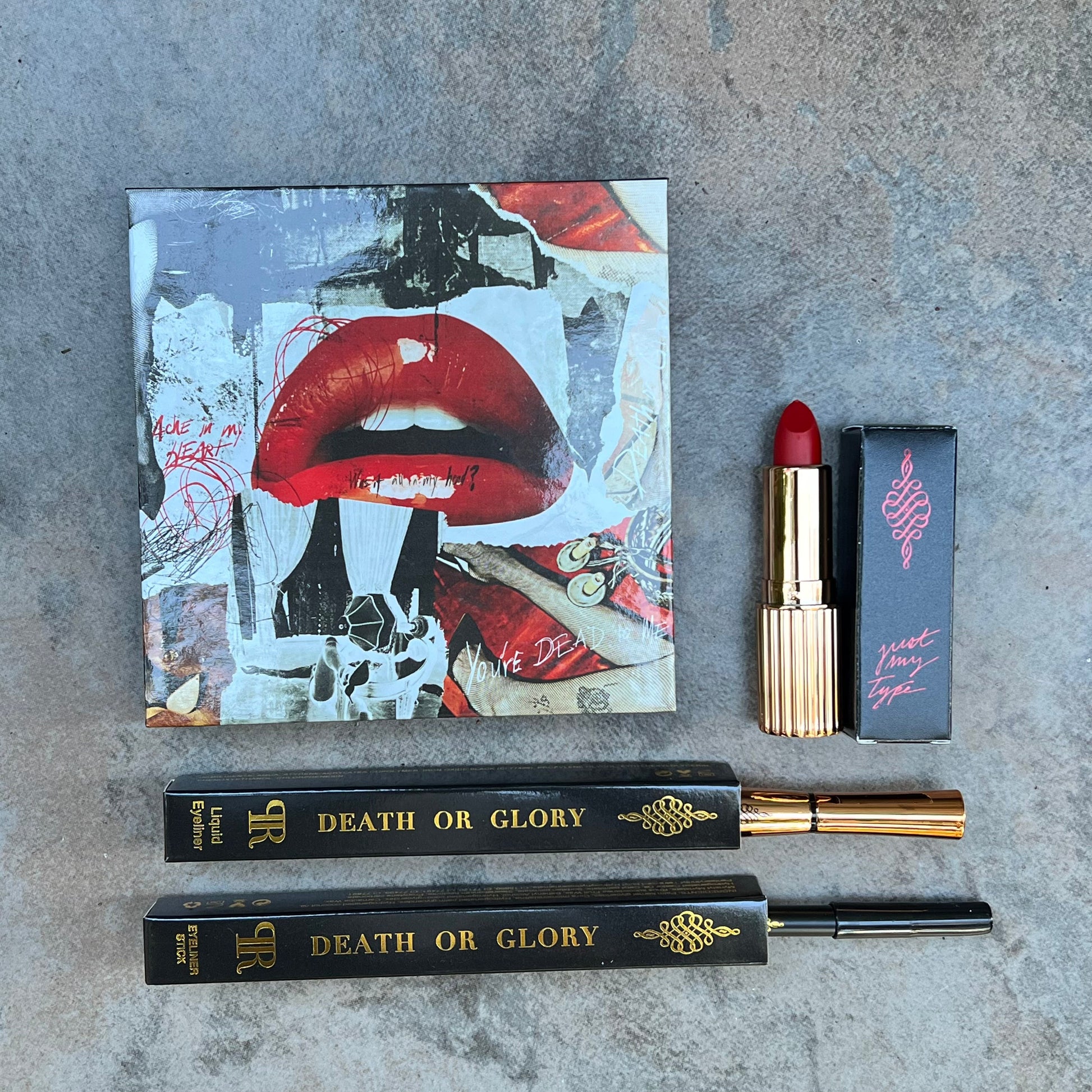Lipstick and lip gloss with 'Death or Glory' packaging on a textured surface