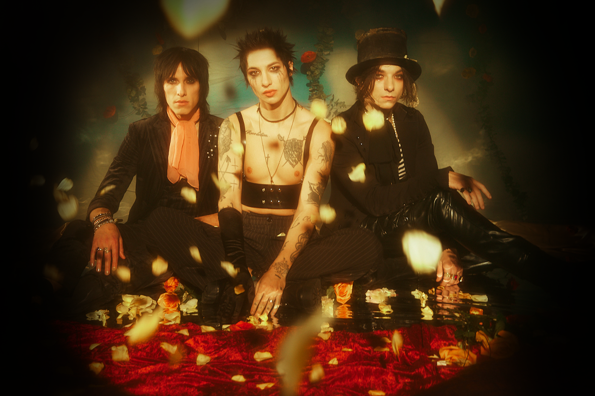 Three individuals in dark, stylish clothing sitting on a red surface with decorative elements.